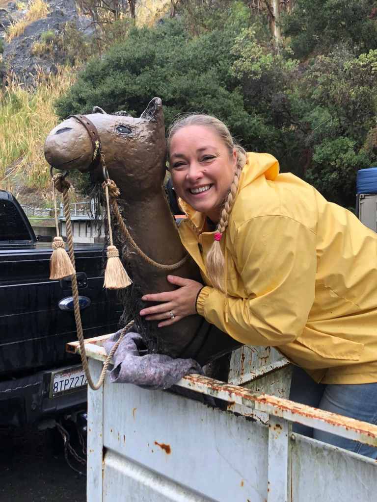 volunteer smiling and posing for photo with camel figure