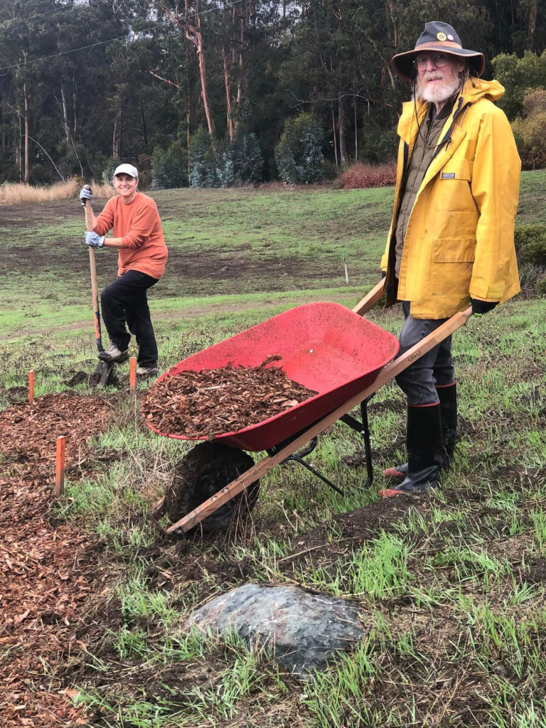 volunteer pushing a wheelbarrow and a volunteer shoveling posing for a photo on set up day
